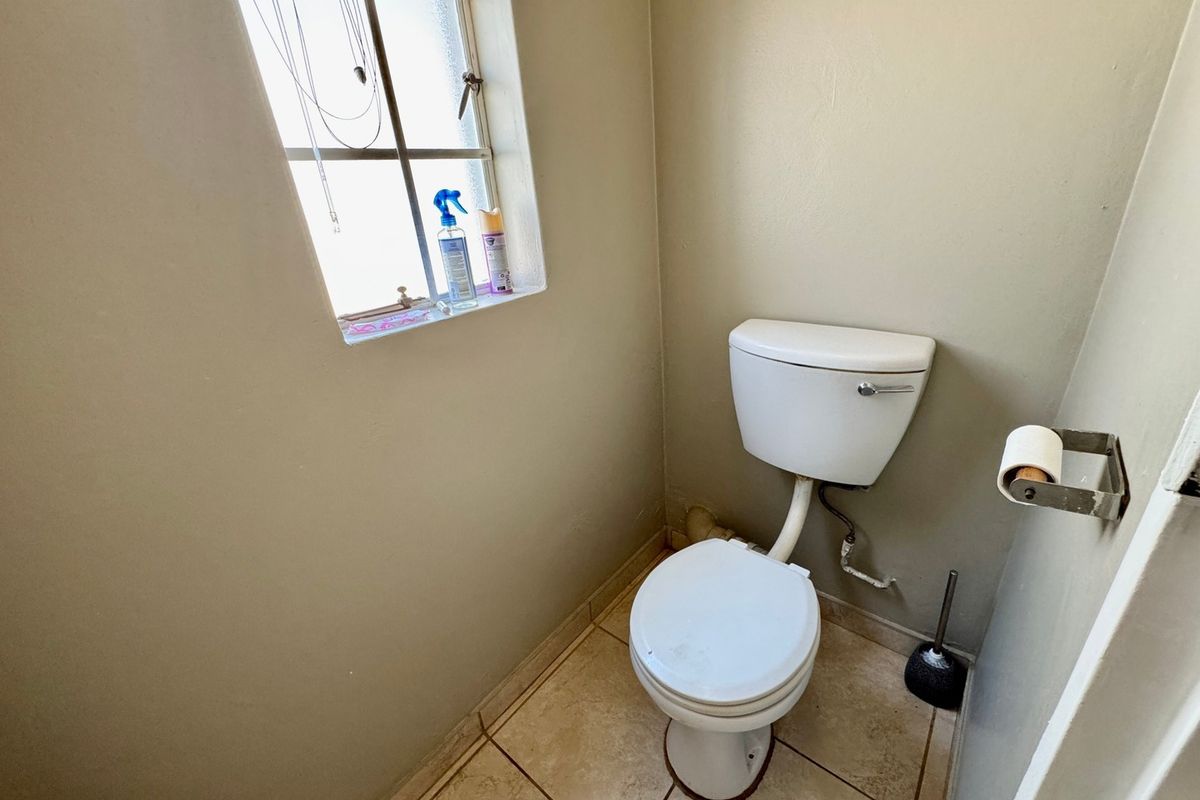 A compact bathroom featuring tiled flooring, a standard toilet, and a window with security bars, requiring minor cosmetic updates.