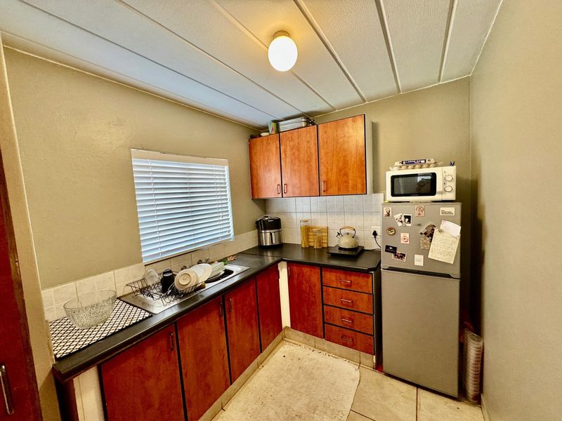 Compact kitchen featuring wood-look cabinetry, dark laminate countertops, tiled backsplash, and tiled flooring, offering a functional layout with potential for modern updates.