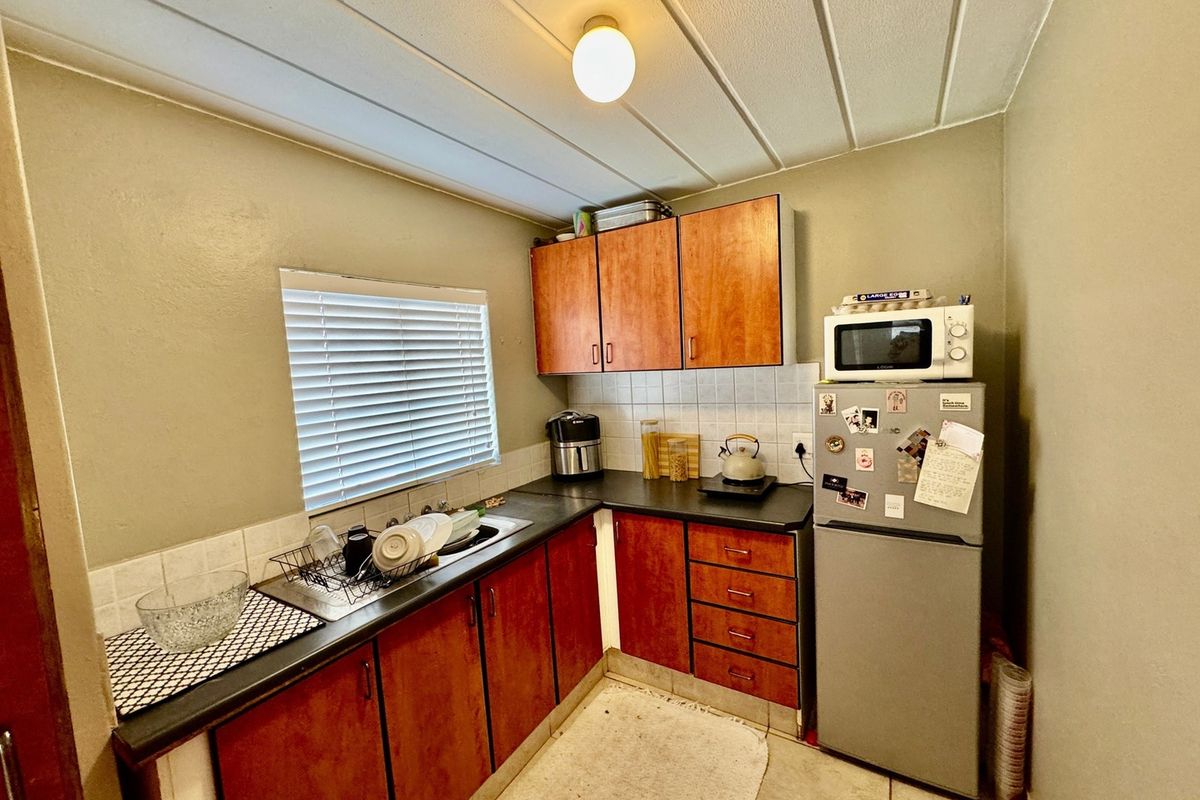 Compact kitchen featuring wood-look cabinetry, dark laminate countertops, tiled backsplash, and tiled flooring, offering a functional layout with potential for modern updates.