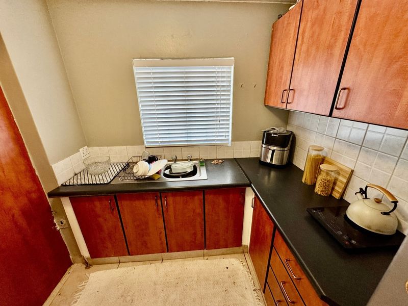 A compact kitchen featuring wood-look cabinetry, dark laminate countertops, a tiled backsplash, and a functional sink area with natural light from a window.