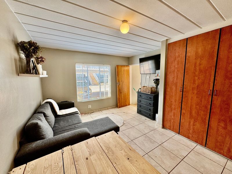 A living room featuring tiled flooring, a slatted ceiling, and built-in wooden cupboards, providing functional storage space within the apartment.