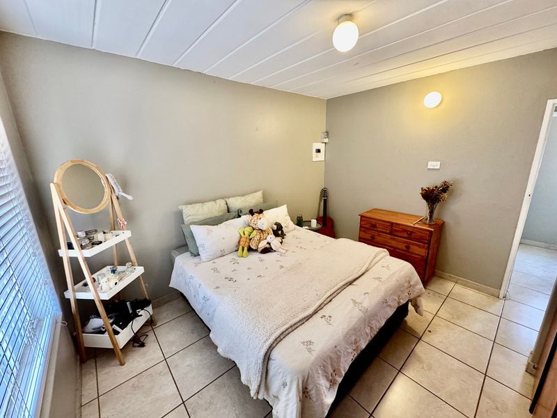 A functional bedroom featuring tiled flooring, a tongue and groove ceiling, and wall-mounted lighting, providing a neutral base for personalization.