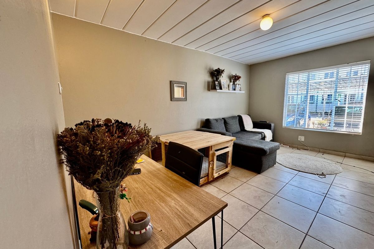 A living room featuring tiled flooring, a slatted ceiling, and a window with blinds, offering a functional space with potential for cosmetic updates.