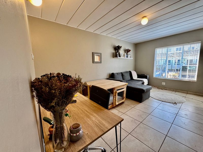 A living room featuring tiled flooring, a slatted ceiling, and a window with blinds, offering a functional space with potential for cosmetic updates.