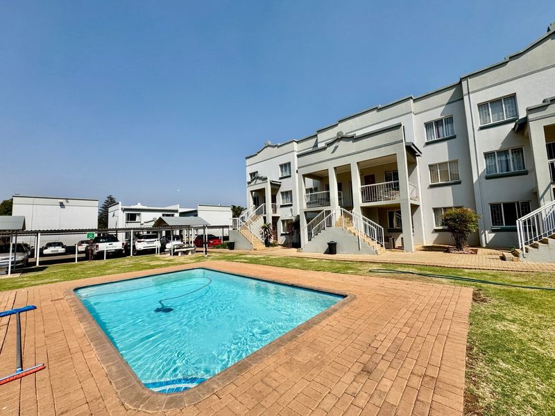 A well-maintained apartment complex featuring a communal swimming pool, paved surrounds, and dedicated covered parking bays.
