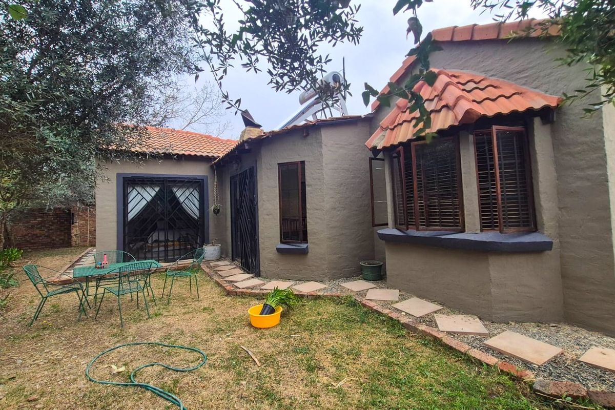 Rear view of the property featuring a textured facade, terracotta roof tiles, a bay window, and a stone pathway leading through the garden.