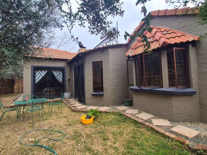 Rear view of the property featuring a textured facade, terracotta roof tiles, a bay window, and a stone pathway leading through the garden.