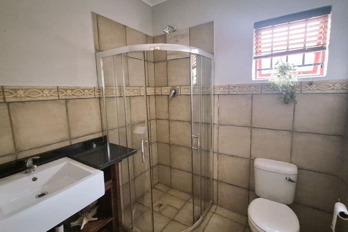 A functional bathroom featuring a corner shower enclosure, vanity basin with granite countertop, and tiled finishes throughout.