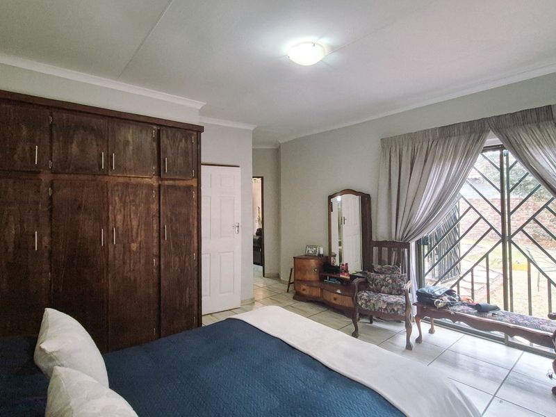 A bedroom featuring built-in wooden cupboards, tiled flooring, and a sliding door with a security gate providing access to the exterior.