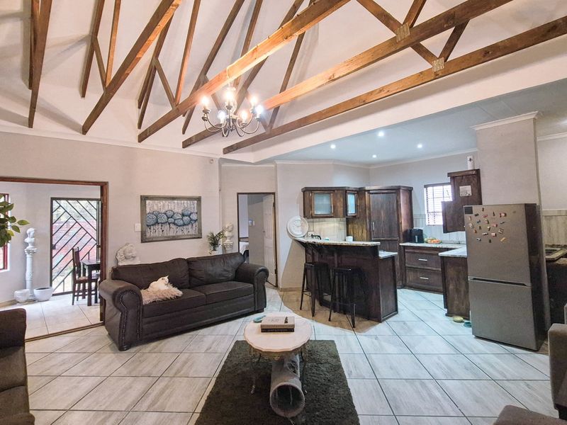 Spacious open-plan living area featuring high vaulted ceilings with exposed timber trusses, tiled flooring, and a functional kitchen with dark wood cabinetry.