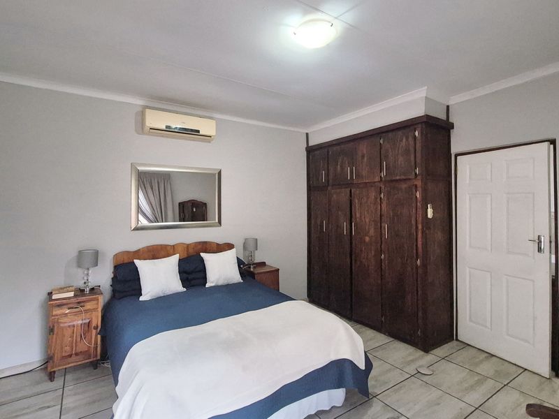 A bedroom featuring tiled flooring, a built-in wooden wardrobe, and a wall-mounted air conditioning unit.