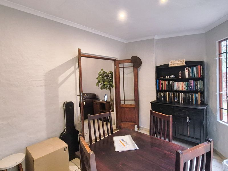 A dining room featuring tiled flooring, coved ceiling cornices, and a timber-framed glass door leading to an adjacent living space.