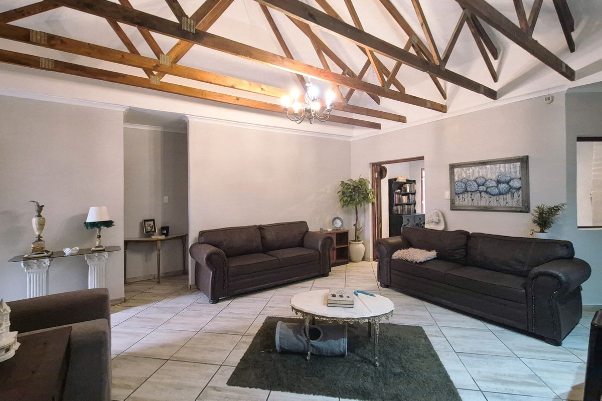 Spacious living room featuring high vaulted ceilings with exposed timber trusses, tiled flooring, and an exposed brick feature wall.