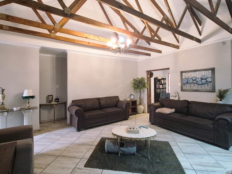 Spacious living room featuring high vaulted ceilings with exposed timber trusses, tiled flooring, and an exposed brick feature wall.