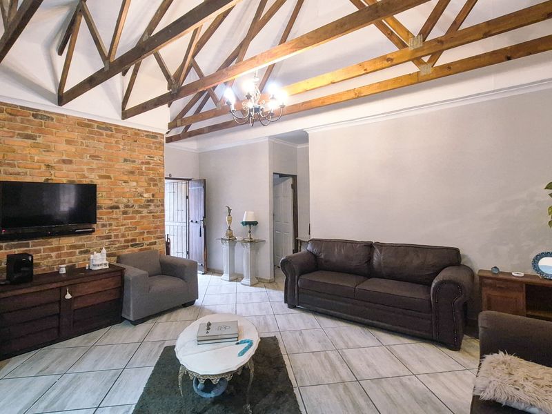 Spacious living room featuring high vaulted ceilings with exposed timber trusses, a rustic brick feature wall, and neutral tiled flooring.