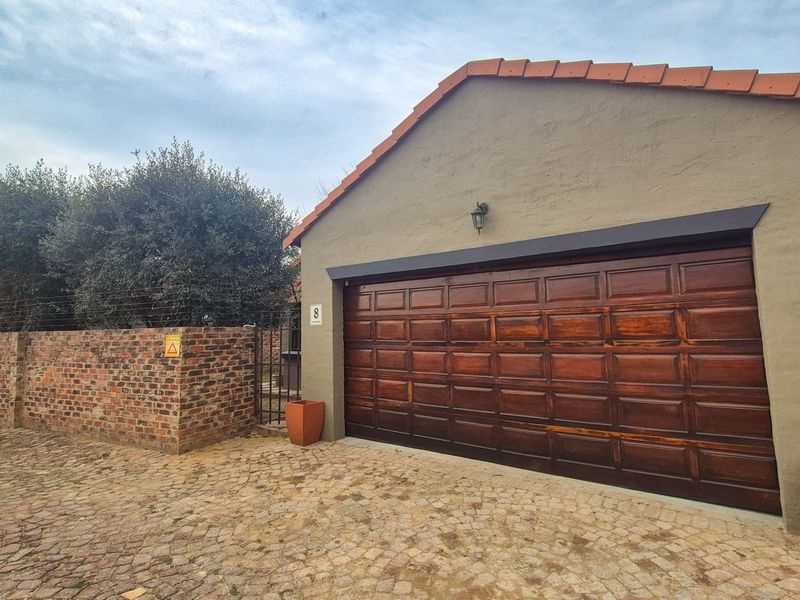 Front exterior view of the property featuring a wooden garage door, cobblestone driveway, and a brick boundary wall.