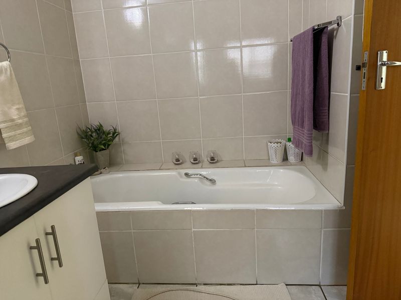 A functional bathroom featuring a built-in bathtub with neutral wall tiling and a vanity cabinet.