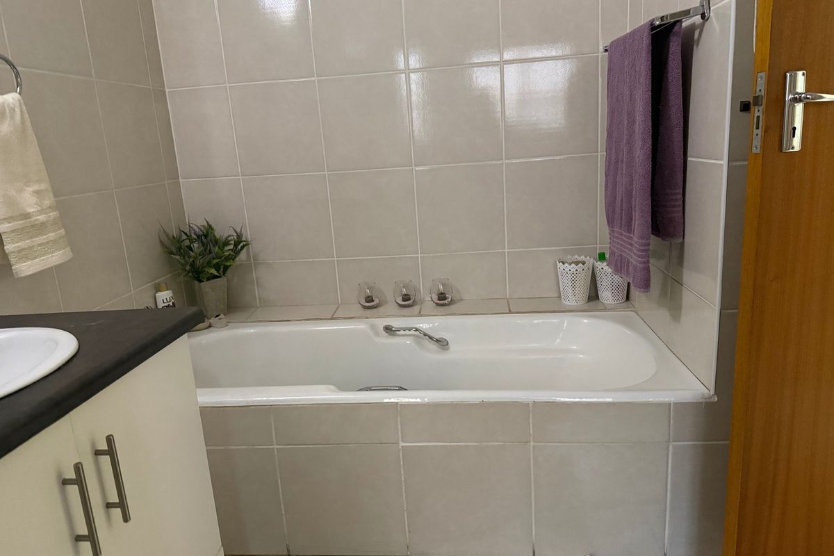 A functional bathroom featuring a built-in bathtub with neutral wall tiling and a vanity cabinet.