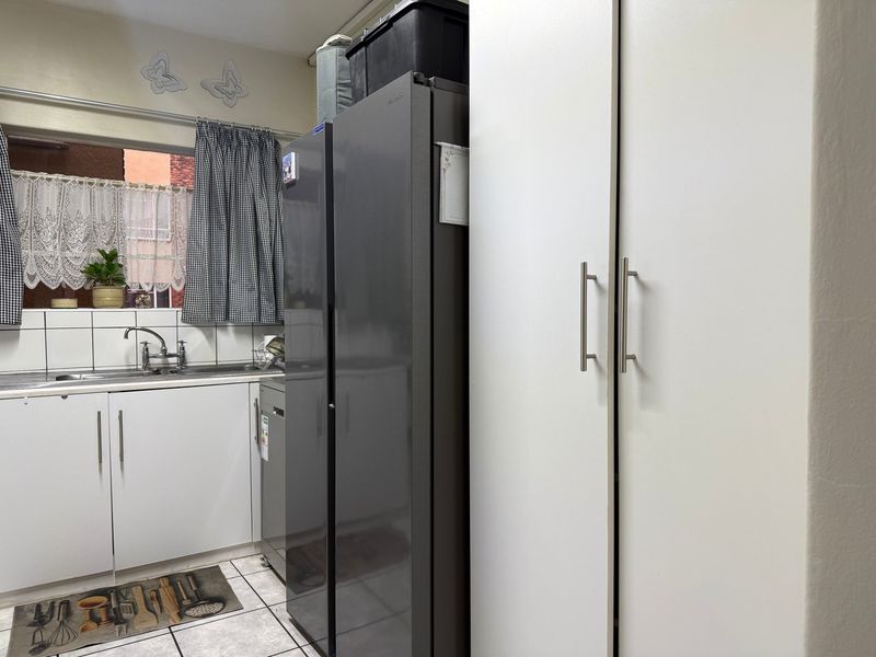 A functional kitchen area featuring white built-in cabinetry, a stainless steel sink with mixer tap, tiled backsplash, and tiled flooring.