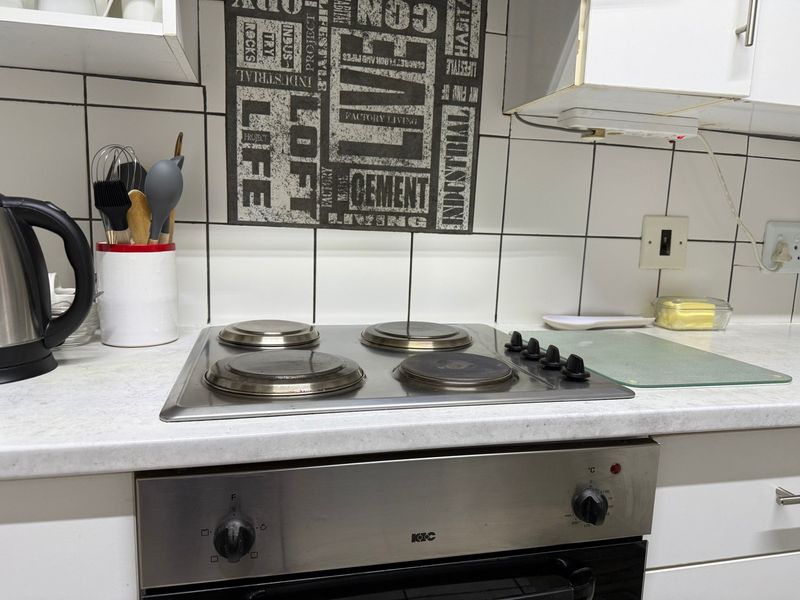A functional kitchen area featuring a built-in oven, electric hob, laminate countertops, and tiled backsplash with overhead cabinetry.