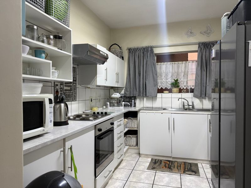 A functional kitchen featuring white cabinetry, laminate countertops, a built-in oven with hob, extractor fan, and tiled backsplash with neutral floor tiles.