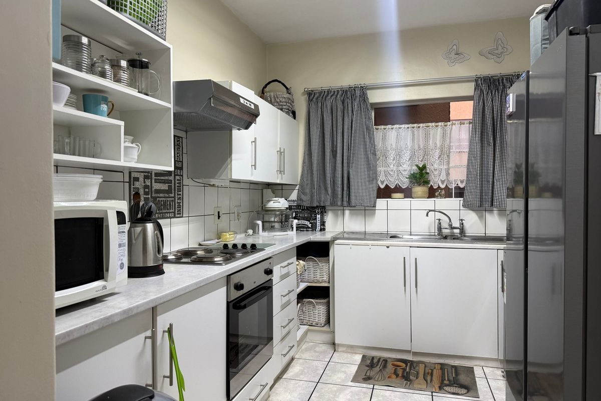 A functional kitchen featuring white cabinetry, laminate countertops, a built-in oven with hob, extractor fan, and tiled backsplash with neutral floor tiles.