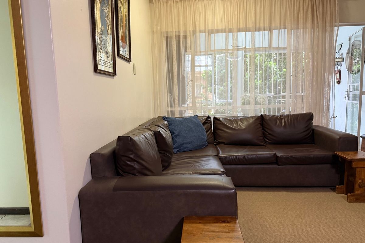 A comfortable living room featuring carpeted flooring and large windows fitted with security bars, allowing natural light into the space.
