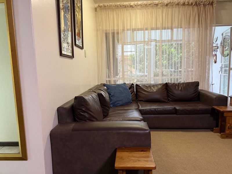 A comfortable living room featuring carpeted flooring and large windows fitted with security bars, allowing natural light into the space.