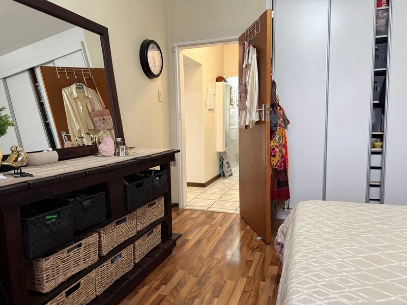 A bedroom featuring laminate flooring and built-in cupboards, with a doorway leading to a tiled hallway.