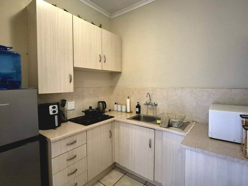 Compact kitchen featuring light wood-finish cabinetry, laminate countertops, a stainless steel sink, and a built-in hob with tiled backsplash.