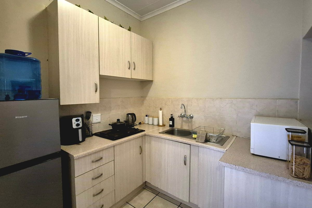 Compact kitchen featuring light wood-finish cabinetry, laminate countertops, a stainless steel sink, and a built-in hob with tiled backsplash.