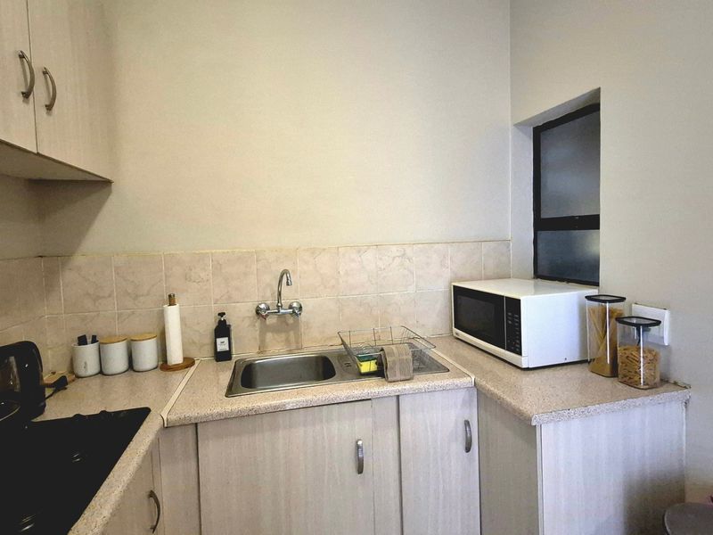 A compact kitchen featuring light-toned cabinetry, laminate countertops, a stainless steel sink, and a tiled backsplash, providing a functional workspace.