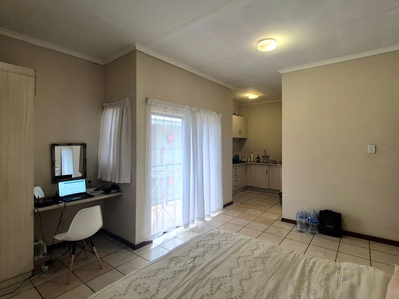 Open-plan apartment layout featuring a bedroom area with built-in storage and desk, leading to a functional kitchen with tiled flooring throughout.