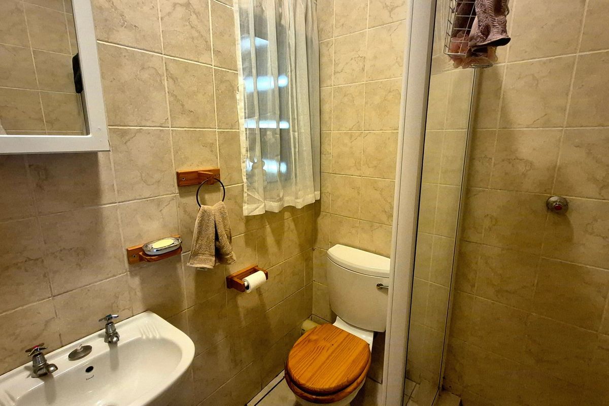 Compact bathroom featuring floor-to-ceiling ceramic tiling, a pedestal basin, a toilet, and a glass-enclosed shower unit.