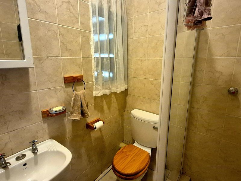 Compact bathroom featuring floor-to-ceiling ceramic tiling, a pedestal basin, a toilet, and a glass-enclosed shower unit.
