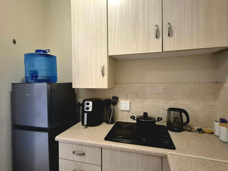 A compact kitchen featuring light wood-finish cabinetry, laminate countertops, a tiled backsplash, and a built-in electric hob.