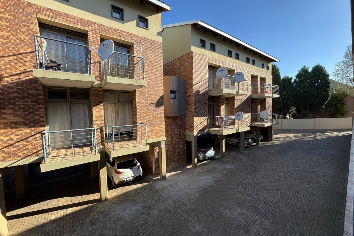 Exterior view of a multi-story apartment complex featuring brick facades, private balconies with metal railings, and ground-level covered parking areas.