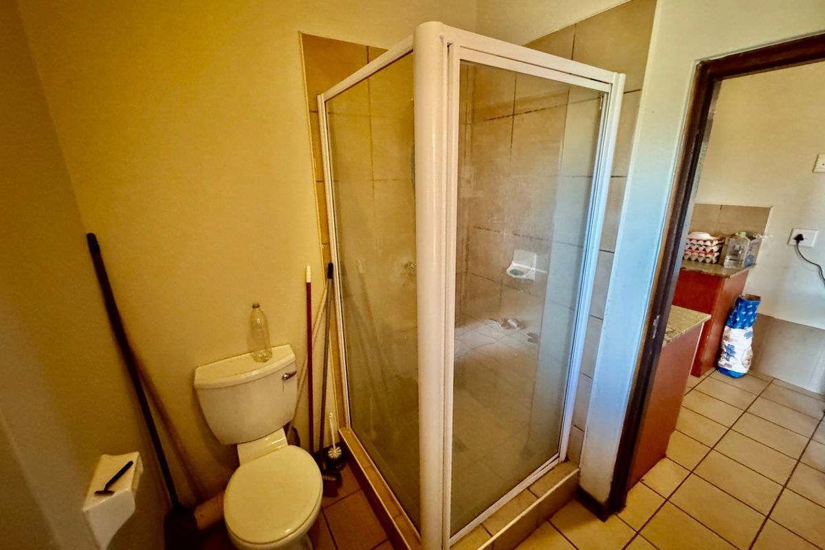 A functional bathroom featuring a corner shower enclosure, toilet, and tiled finishes, requiring cosmetic updates to improve its overall condition and appeal.