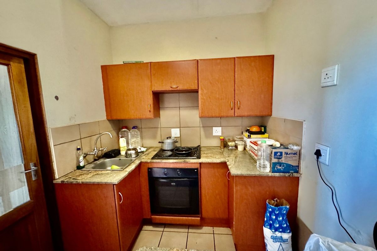 Compact kitchen featuring laminate cabinetry, stone countertops, built-in oven, and electric hob with tiled backsplash and flooring.
