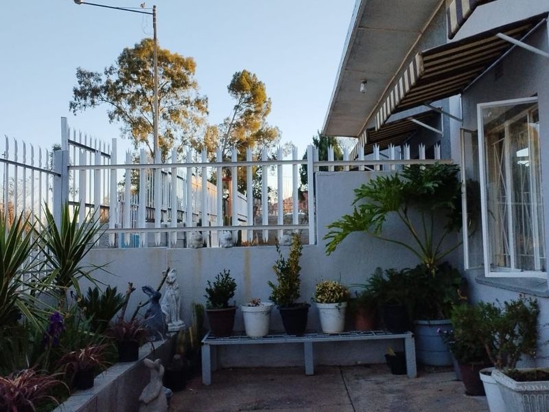 A paved patio area featuring a retractable awning, boundary wall with security spikes, and established garden elements.