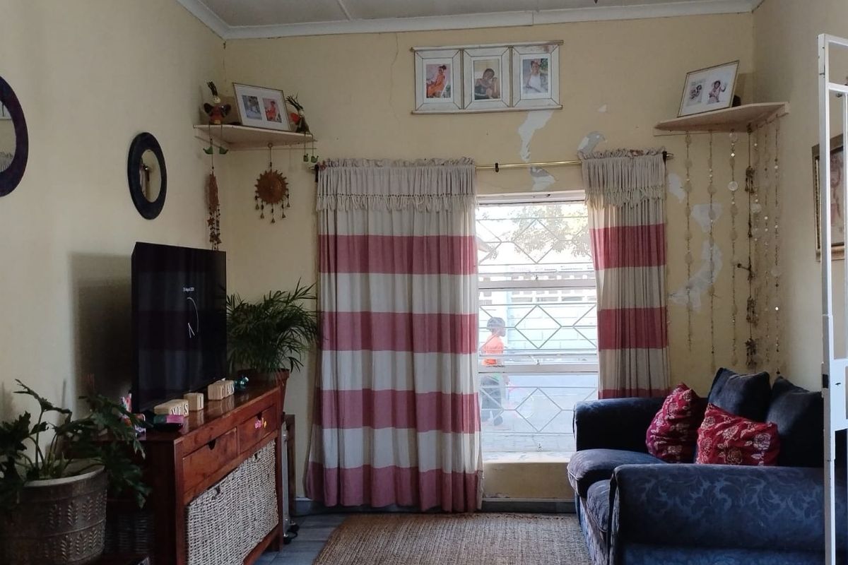 A living room area featuring a window with security bars and a security gate, showing signs of wall surface deterioration.