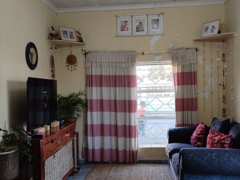 A living room area featuring a window with security bars and a security gate, showing signs of wall surface deterioration.