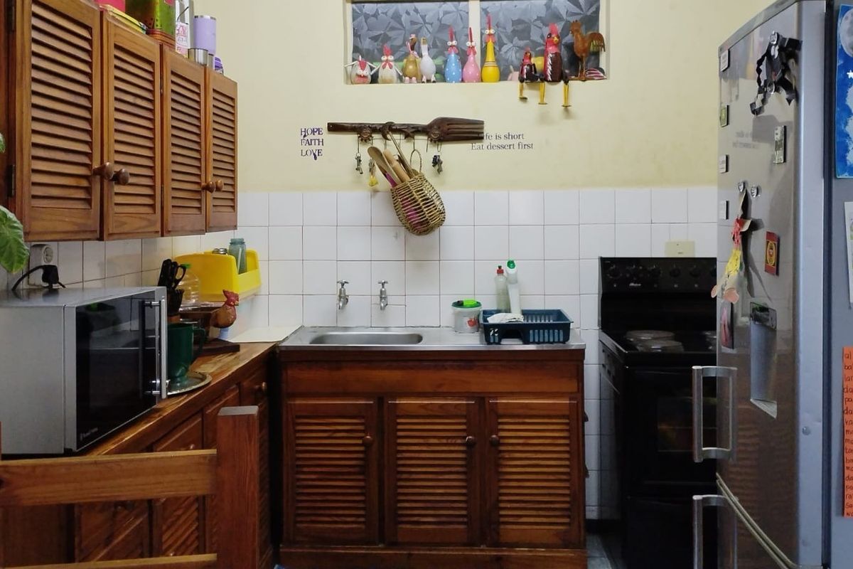 A compact kitchen featuring traditional wooden louvered cabinetry, a stainless steel sink, tiled backsplash, and a freestanding oven.