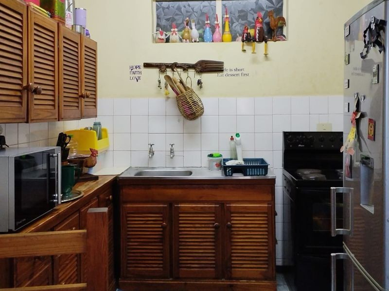A compact kitchen featuring traditional wooden louvered cabinetry, a stainless steel sink, tiled backsplash, and a freestanding oven.