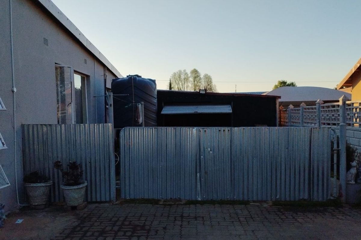 Rear exterior view of the townhouse featuring a paved area, corrugated metal fencing, and a water storage tank.