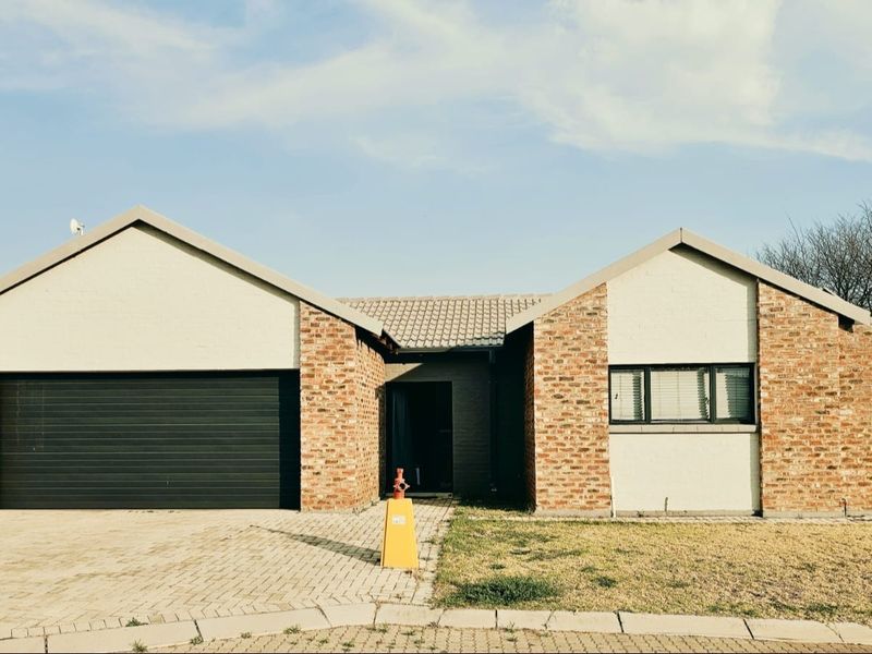 Front view of a single-story brick house featuring a double garage, paved driveway, and a central entrance.