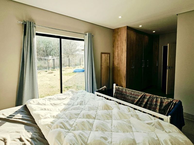Spacious bedroom featuring built-in wooden cupboards, modern tiled flooring, recessed lighting, and a large sliding glass door providing direct access to the garden.
