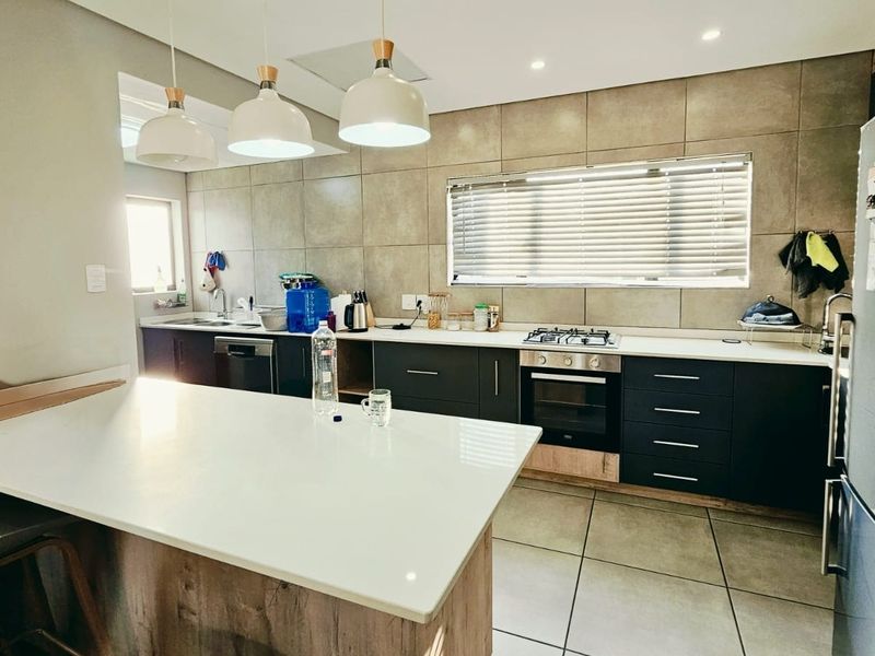 Modern kitchen featuring dark cabinetry, stone countertops, a central island, and integrated appliances with contemporary tiled finishes and stylish pendant lighting.
