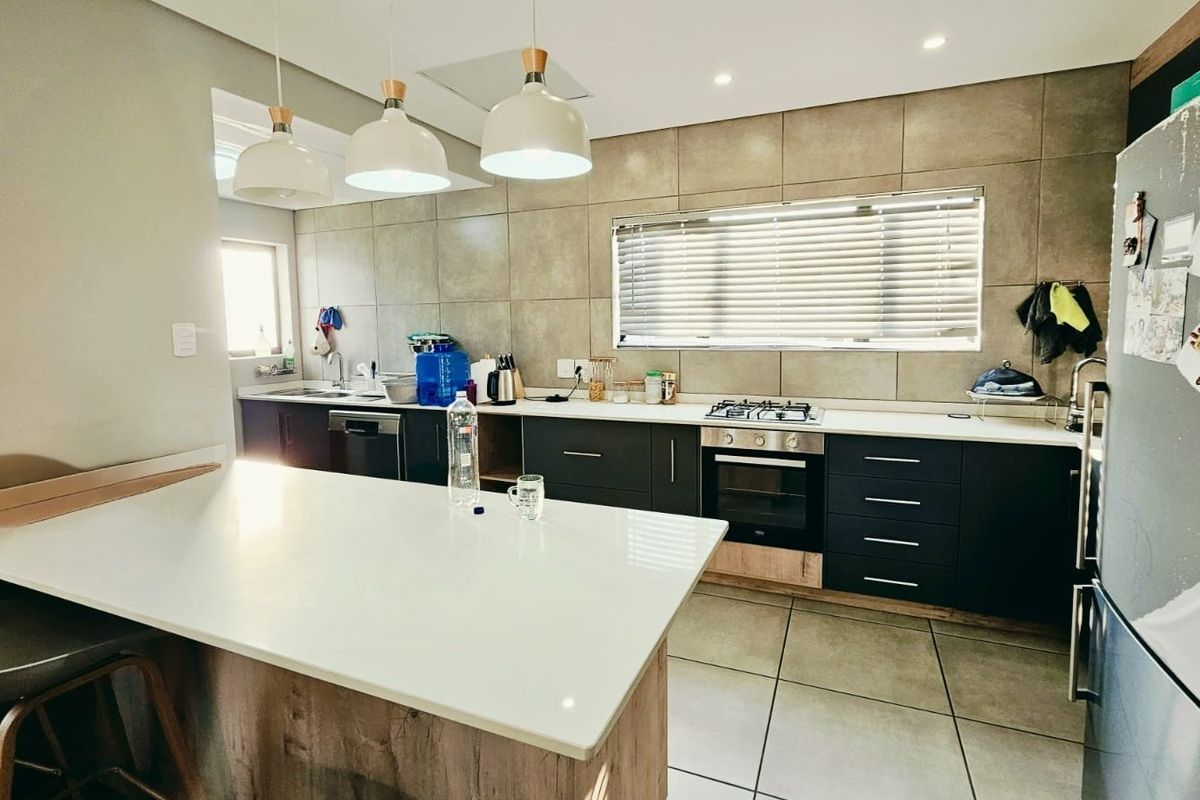 Modern kitchen featuring dark cabinetry, stone countertops, a central island, and integrated appliances with contemporary tiled finishes and stylish pendant lighting.