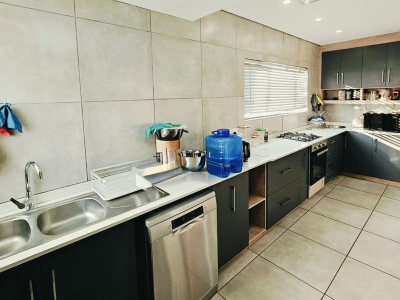 Modern kitchen featuring dark cabinetry, stone countertops, a double sink, built-in oven, gas hob, and large format floor tiles.